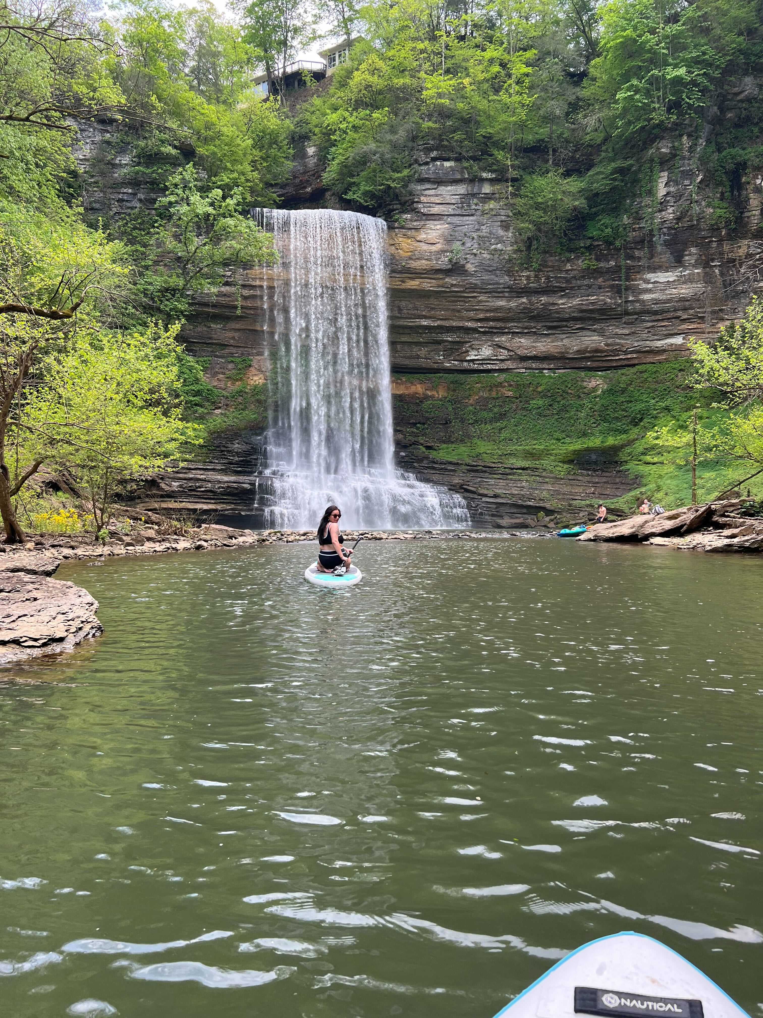 Girl paddle boarding in front of a waterfall.